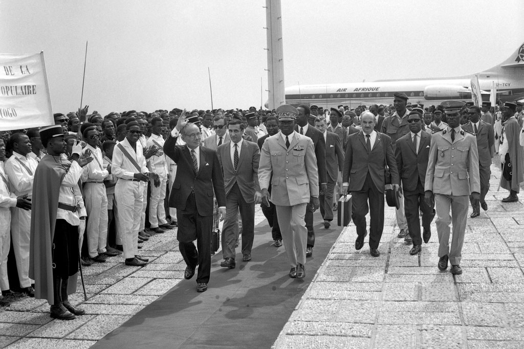 Secretary-General U Thant greets the gathering that welcomed him upon his arrival in Togo in January 1970. At right is the President of Togo, Etienne Eyadama. At centre is Jean Gazarian, Senior Officer, Executive Office of the Secretary-General. UN Photo