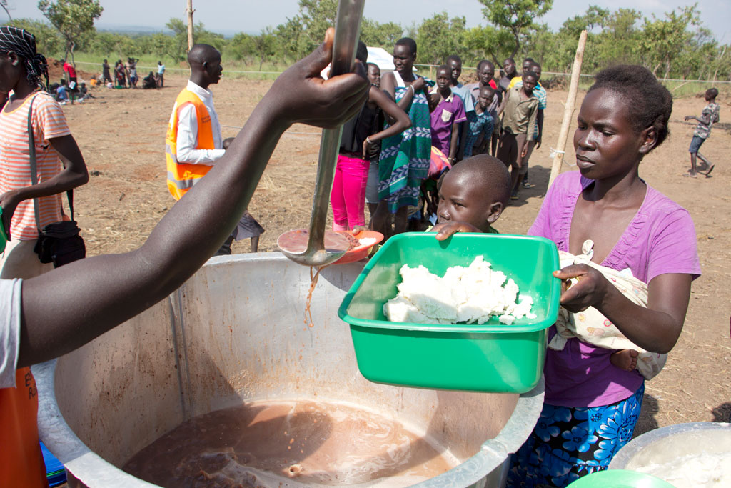 A woman being served a hot, fortified maize meal with beans to share with her children. Like all new refugee arrivals, they will depend on the UN WFP for such meals until they can support themselves, a long time from now. Photo: WFP/Henry Bongyereirwe