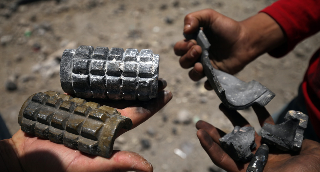 Children hold shrapnel from exploded artillery shells while standing on a street damaged by blasts in Sana’a.