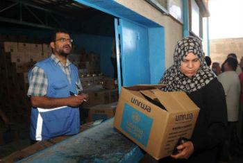 Funcionário da agência entrega alimentos a mulher refugiada. Foto: Unrwa/Shareef Sarhan